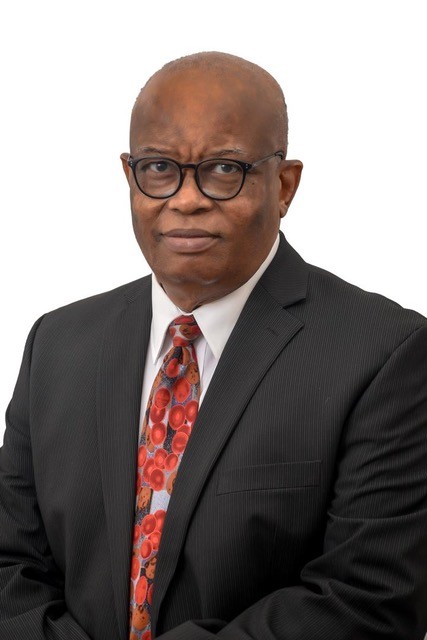 A man wearing glasses, a black suit, white shirt, and a colorful patterned tie, posing against a white background.